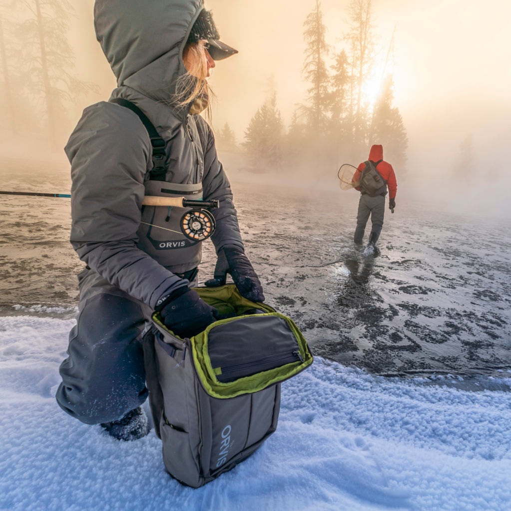 The sun rises on an icy foggy morning with two anglers in full insulated gear.