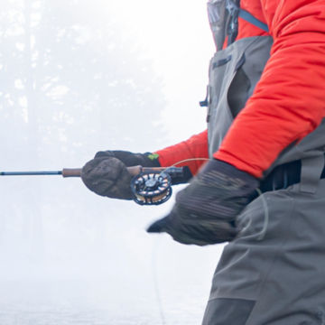 Angler wearing PRO Insulated Convertible Mitts wades through an icy river.