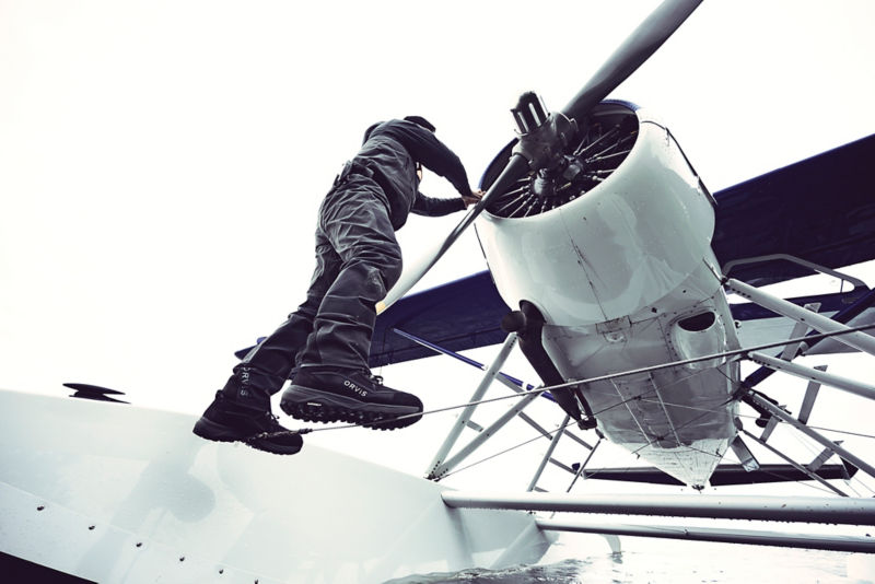 A man wearing waders climbing over the pontoon of a float plane.