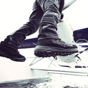 A man balances under a biplane over the water with waders and wading boots on.