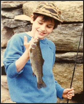 Jeff as a boy, fishing pole in hand as he holds up a trout he caught.