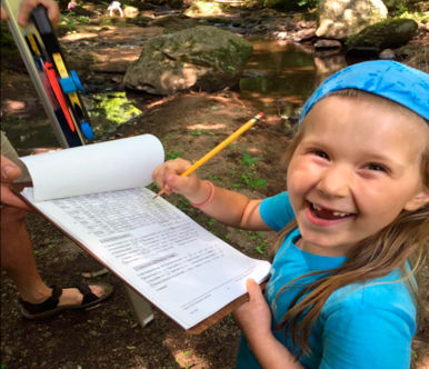 A young girl smiles while filling out records on a clipboard.
