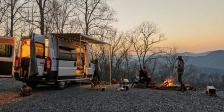 A family around a fireplace near their camper at sunset