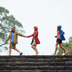 Three people walking in a row on ruins wearing rain coats