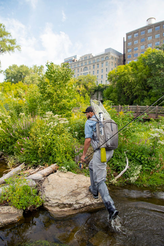 Man walks along bridgehead in his Ultralight Wading Boots carrying fishing gear.