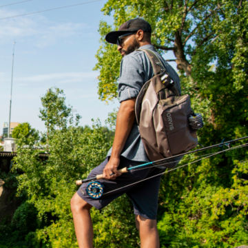 Angler wearing Orvis Guide Sling Pack overlooks river and plans the walk down to the shore.
