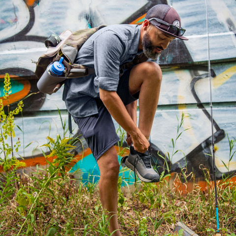 An angler ties their shoe with graffiti in the background