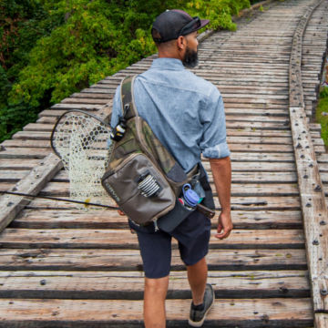 Angler with Sling Pack walks down railroad tracks.