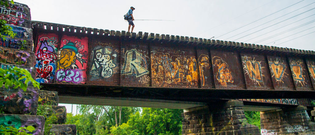 A view from below of an angler walking across a railroad bridge that is covered in colorful graffiti