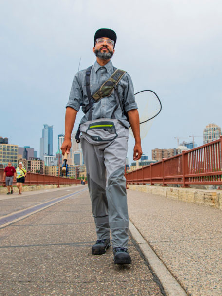 Man walks along bridgehead in his Ultralight Wading Boots carrying fishing gear.