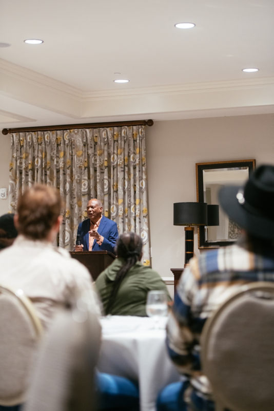 A speaker at a podium can be seen gesturing through the crowd of people