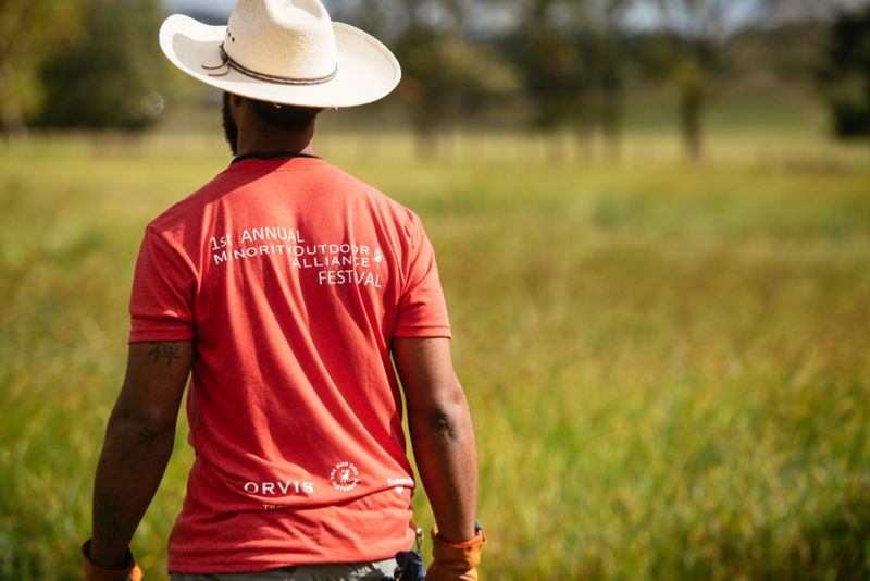 Durrell Smith walking away from the camera, wearing a red t-shirt with "1st Annual Minority Outdoor Aliance Festival" written on the back.