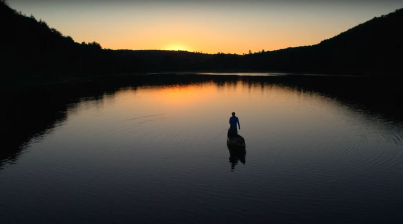 An aerial view of a man fishing in a lake at sunset.