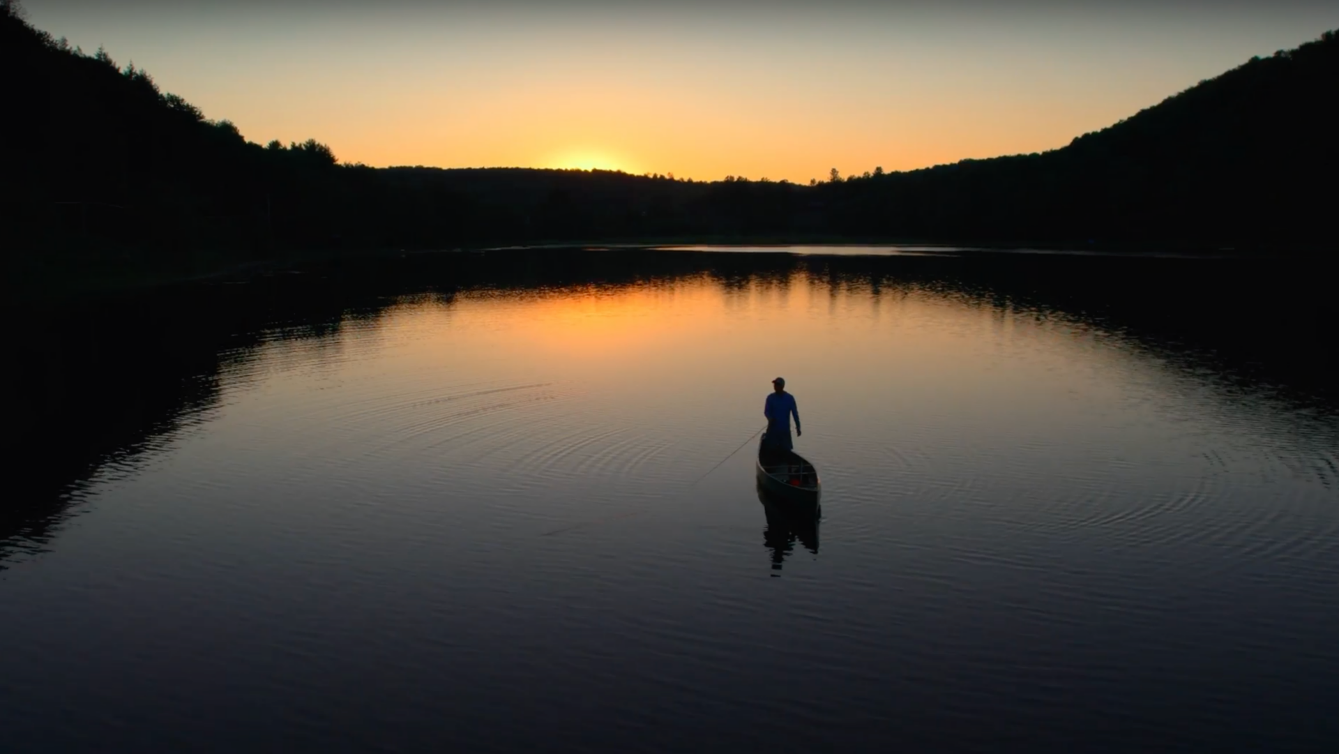 An aerial view of a man fishing in a lake at sunset