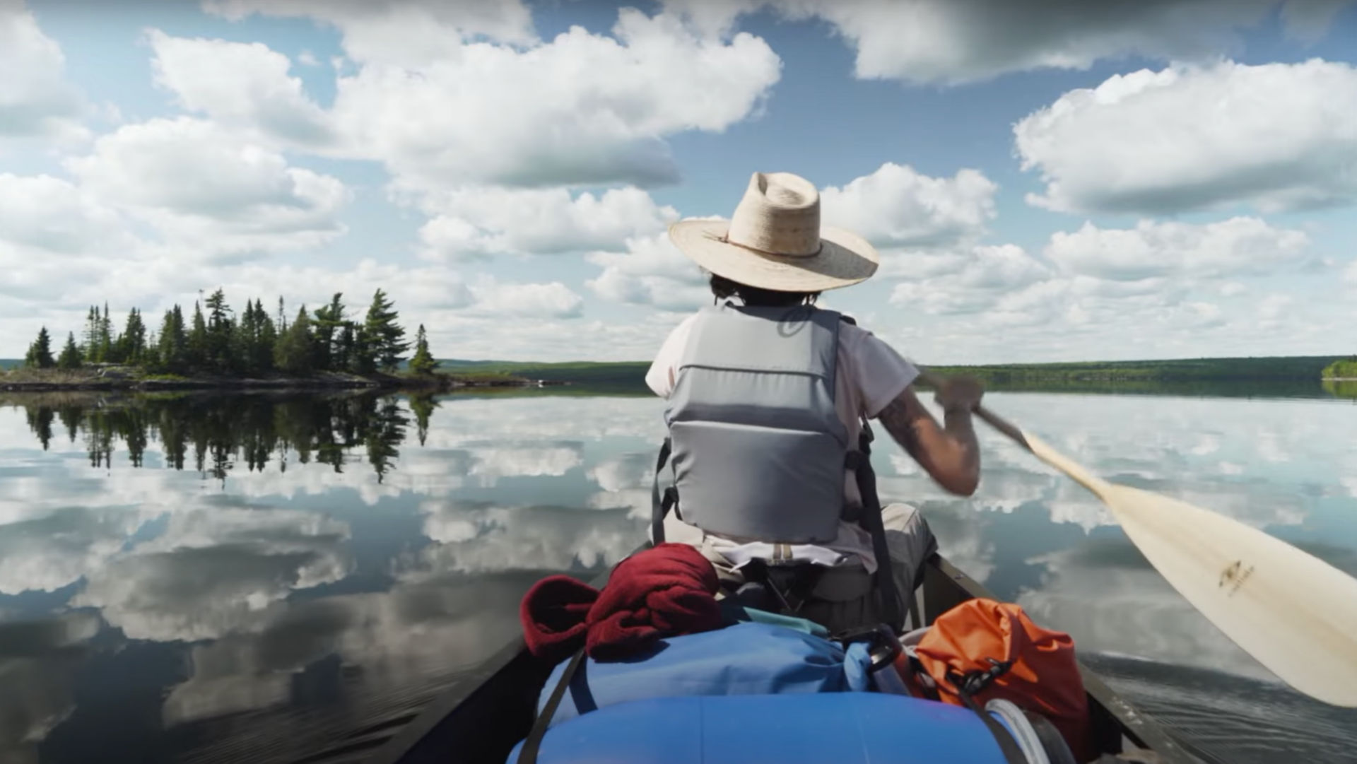 Looking at a person from behind while they paddle a canoe on a lake