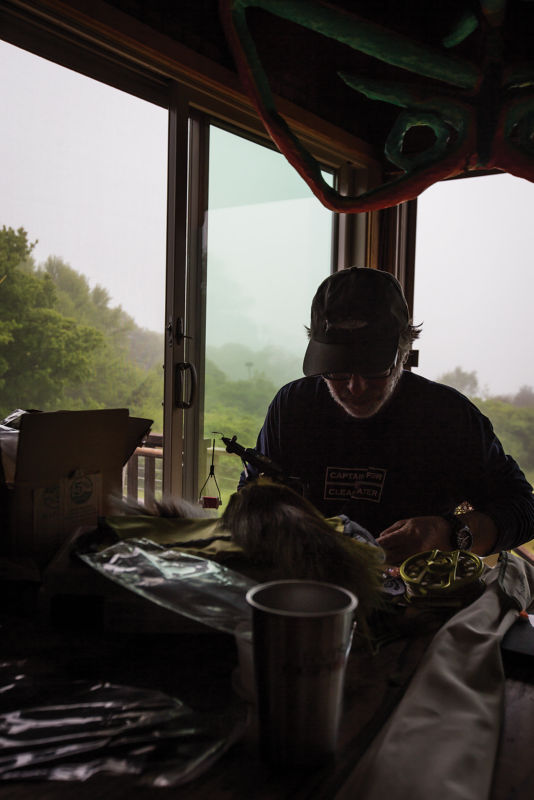 Tom in silhouette, tying flies at his desk.