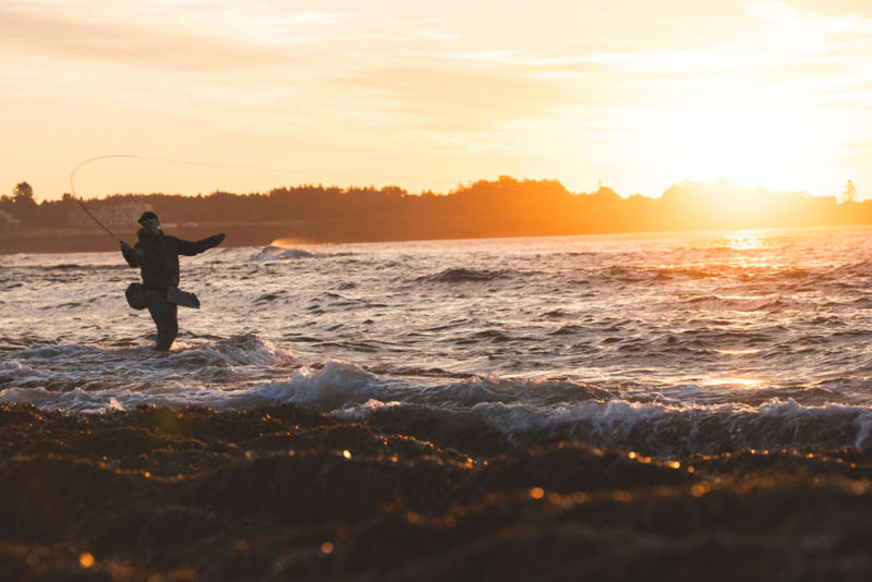 An angler pulls back his rod for his next cast while wading in the surf.