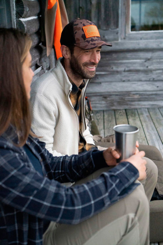 Two people relaxing on a gray wood porch of a log cabin.
