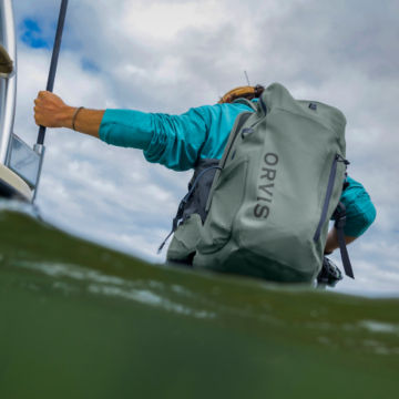 Angler wearing PRO Waterproof Backpack 30L wades through the water to their boat.