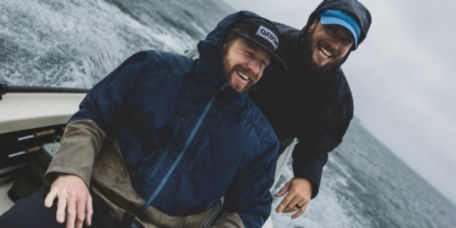 Two anglers wearing rain jackets manage to laugh about the miserable, rainy weather