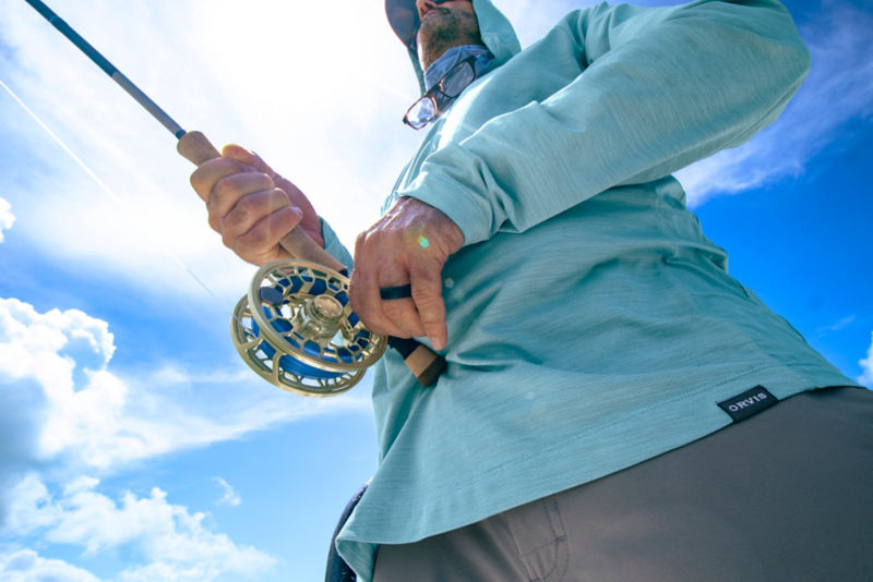 A close view of the hands of an angler as they work a gold Ratio fly reel on their fly rod.