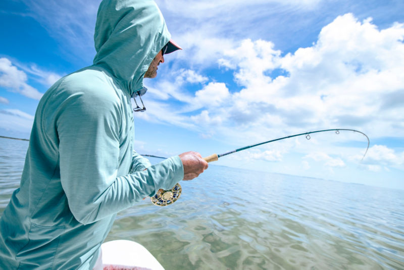 A closeup of a hand holding a fly rod with the silver and blue reel showing.