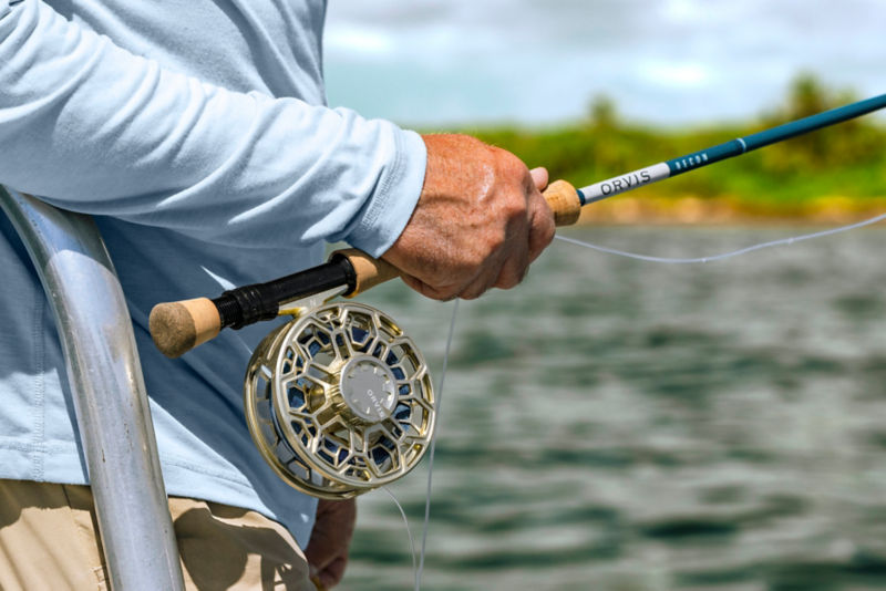 A close-up of an angler holding a fly rod with the gold Ratio Fly Reel.