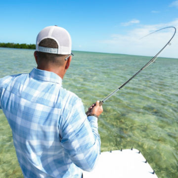 An angler on a salt flat casts his Helios rod from a skiff.