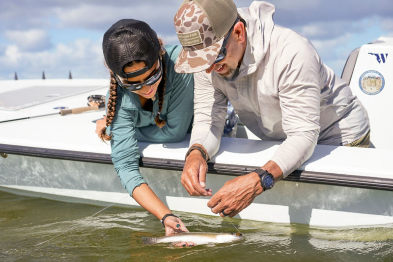 Two anglers leaning over the side of the boat holding the fish they caught.