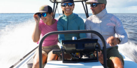 Three people crowd together on a motorboat speeding through the ocean.