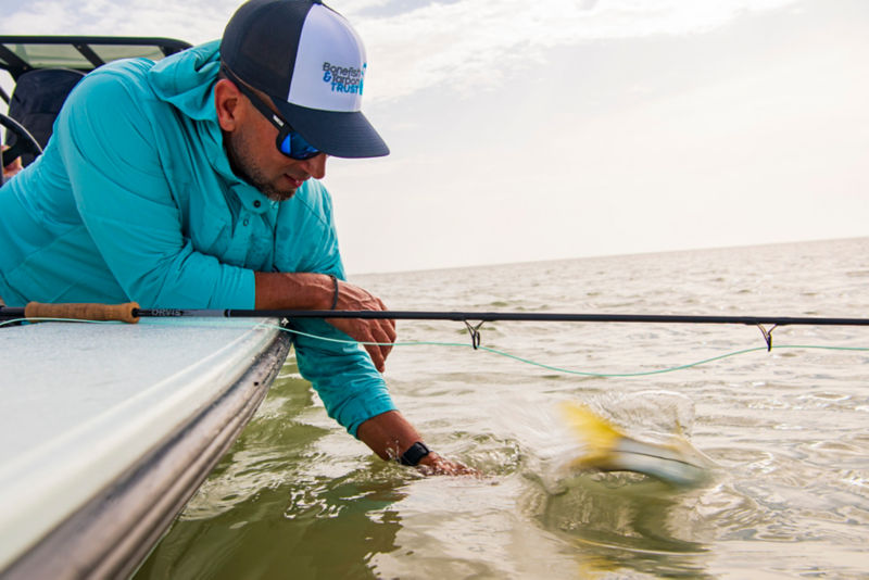 An angler in robin's egg blue leans over the side of a craft to release a fish