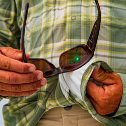 An angler cleans their sunglasses with the chamois material on their shirt