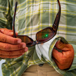 An angler cleans their sunglasses with the chamois material on their shirt