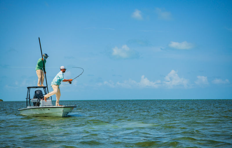 A skiff poled by one angler while another angler casts his fly rod.