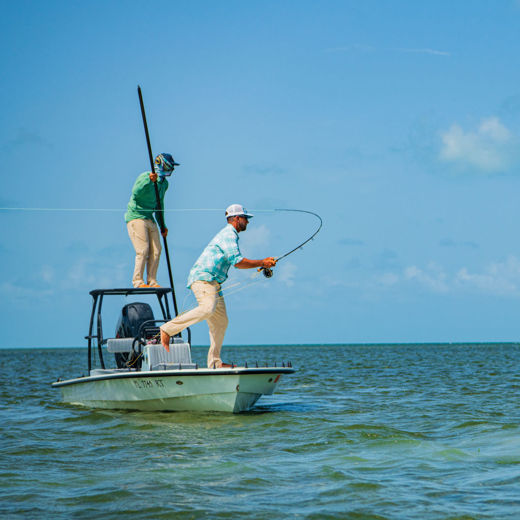 An angler's rod bends as they cast from the bow of a small ocean watercraft.