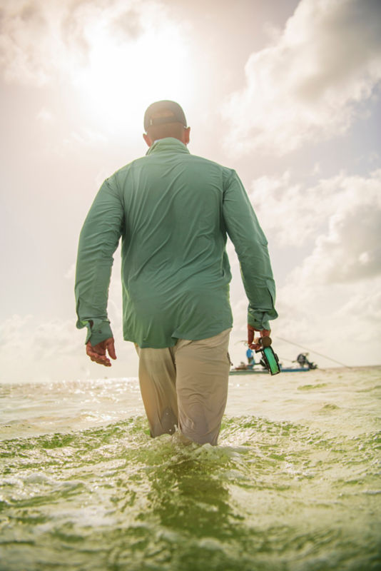 An angler walks through the surf toward a boat.