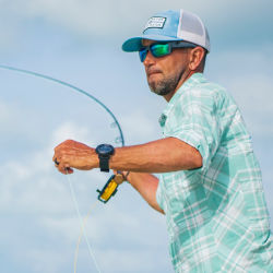 A man wearing a hat and checked shirt casting a fly rod into the water