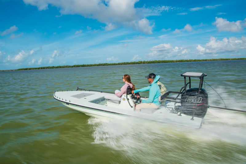 Three people speed by in a small boat on a beautiful day.
