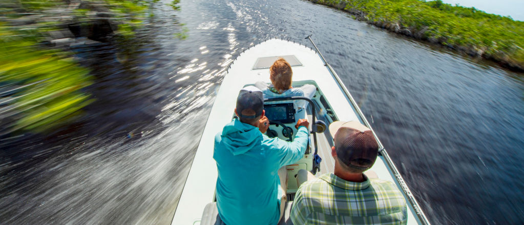 Three people speed down the Kissimmee River in a sleek motor boat
