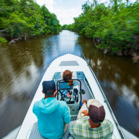 Three anglers in a speeding boat riding through the everglades, seen from behind