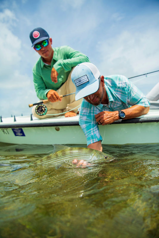 Two anglers release a fish over the side of a boat back into the ocean