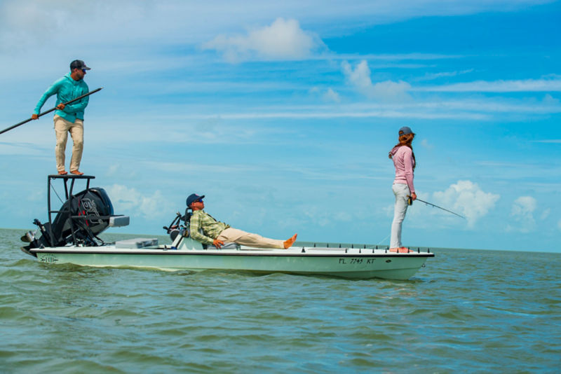 Three people fishing off a small boat on a green ocean