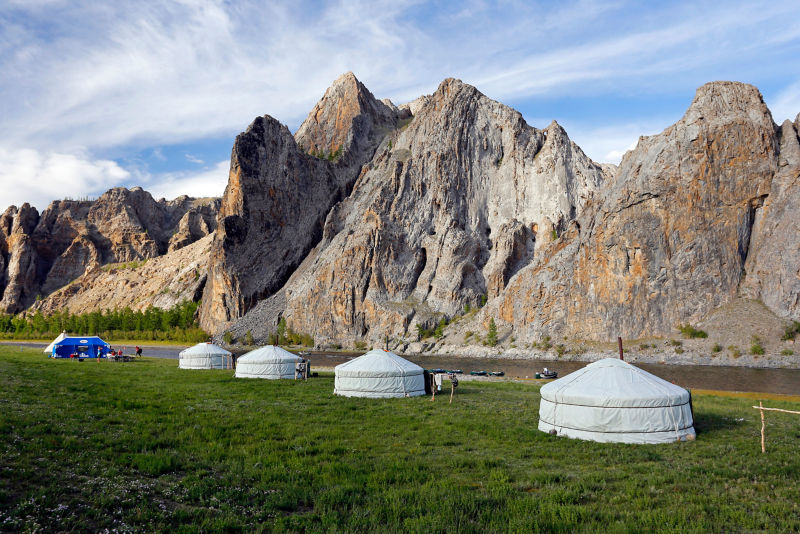Several Yurts sitting on a grassy field by mountains in Mongolia.