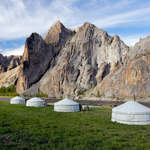 Several Yurts sitting on a grassy field by mountains in Mongolia.