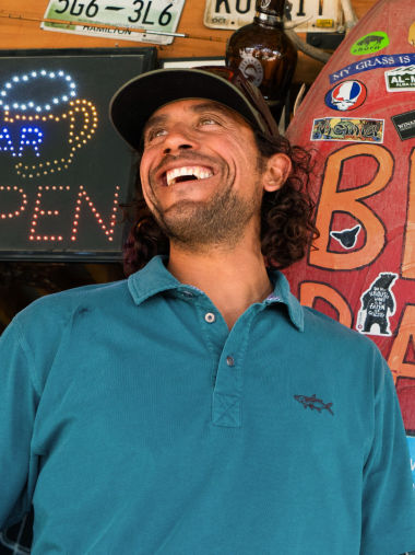 A smiling man wearing a teal angler polo and ball cap.