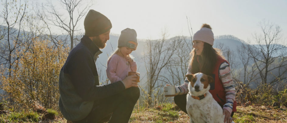 A family and their dog in the early morning with mountains and fog as the backdrop