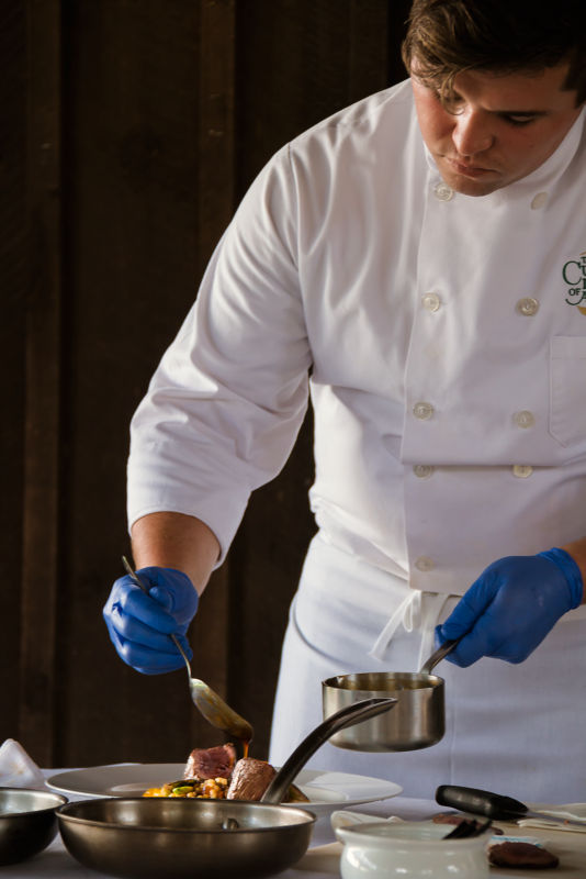 A chef wearing white demonstrates game cooking.