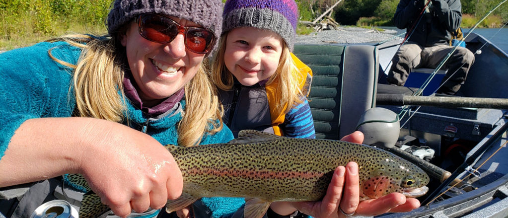 Nelli Williams shows off a fresh-caught fish with her small child grinning behind her.