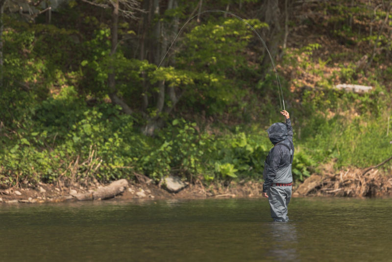 An angler casts while standing in a shallow river.