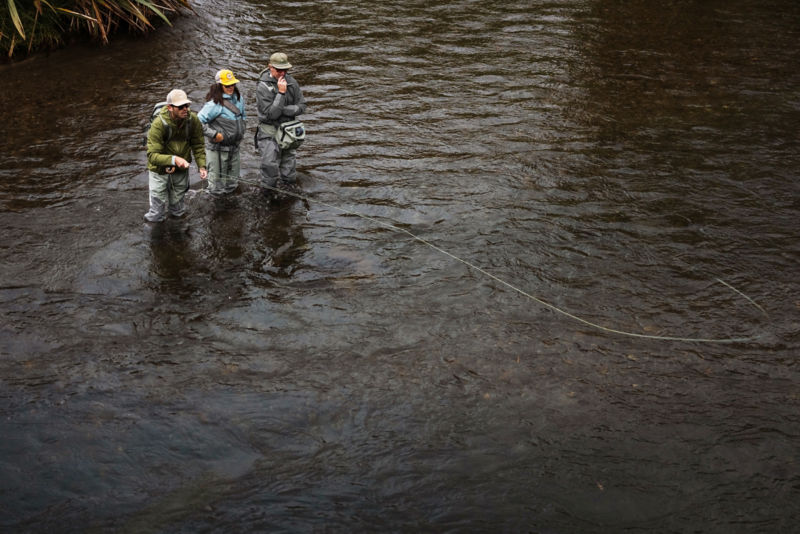 Two anglers in waders fish from a rocky stream bed.